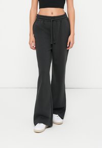 Pantalons de survêtement noires évasés avec une taille élastique et un cordon de serrage. Tissu doux, deux poches latérales, et un discret logo sur la cuisse.