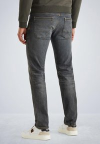Jean en denim gris à coupe ajustée, avec un design à cinq poches et des coutures sur les poches arrière. Associé à des baskets blanches et un sweat-shirt gris.
