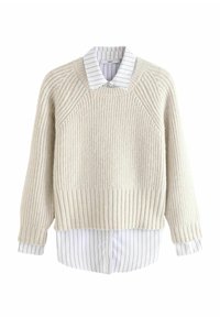 Cremefarvet ribstrikket sweater med raglanærmer, lagdelt over en hvid og stribet skjorte med forskellige tekstiler.