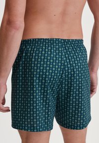 Shorts de bain pour homme en turquoise foncé avec un motif géométrique en bleu clair et vert. Taille élastique et tissu léger.