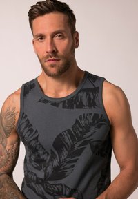 Šedý bezrukávový top s černým vzorem listů, vyrobený z měkké tkaniny s hladkou texturou a kulatým výstřihem.