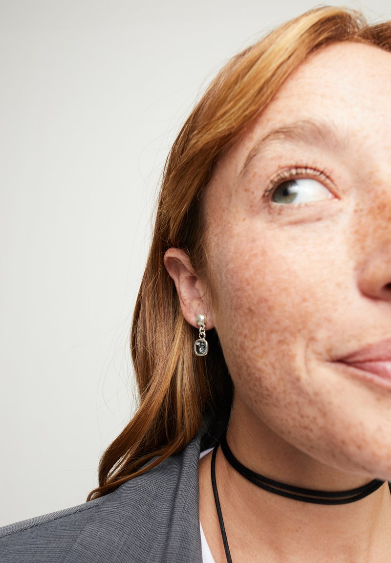 Pendientes de plata que presentan un botón circular de perla y un colgante rectangular con una piedra oscura. Superficie lisa, diseño colgante y detalles discretos.