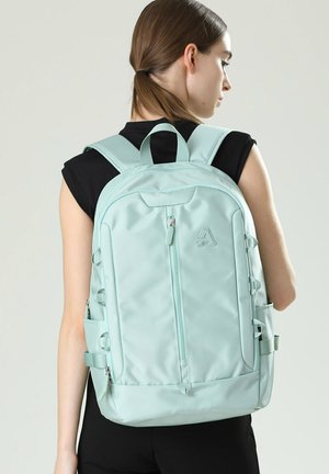 Light blue backpack with adjustable straps, front zip pocket, side loops, and textured material, suitable for casual or travel use.