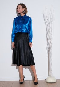 Blue satin blouse with a bow tie neck, paired with a black satin midi skirt. Accessories include large earrings and black high heels.