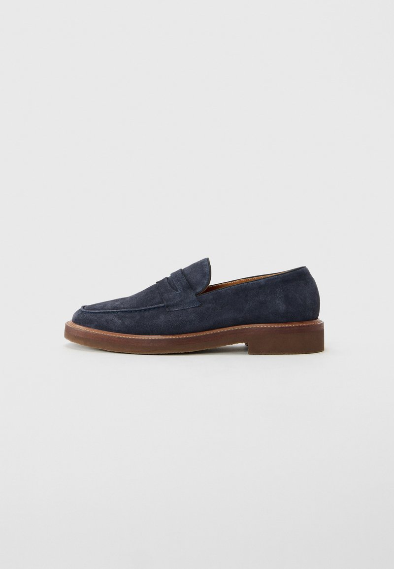 Mocassin en daim bleu marine avec une semelle marron et un petit talon, arborant un design classique de bandeau en penny.
