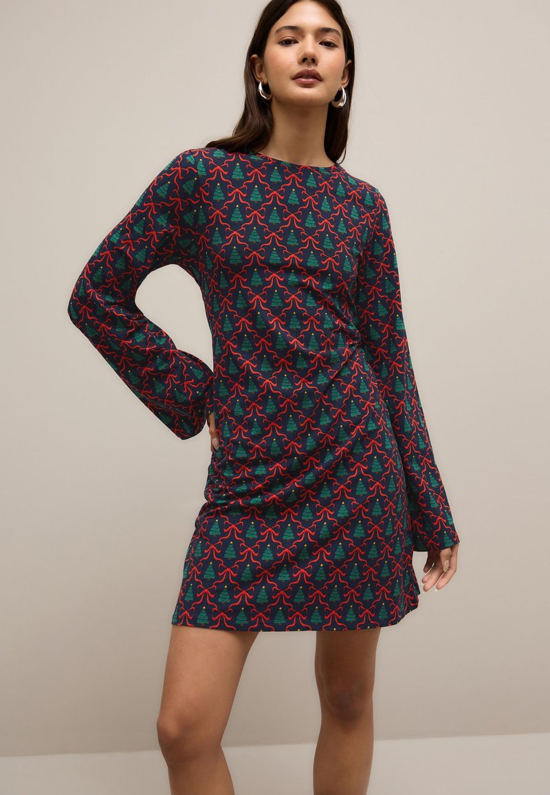 Robe colorée à motifs avec manches longues présentant un design d'arbre vert et de nœud rouge sur un fond sombre ; tissu lisse, silhouette ajustée.