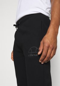 Svarta sweatpants med elastisk midja och snörning. Har sidfickor och en tonad logotypdetalj nära vänster höft. Mjuk tygkvalitet.