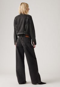 Svart denimjakke med en kort design og lange ermer, kombinert med vide svarte jeans med en tan label og klassiske lommer.