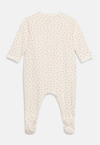 Ολόσωμη φόρμα μωρού σε κρεμ χρώμα με μακριά μανίκια, καλύμματα ποδιών και μικρά κόκκινα μοτίβα καρδιάς σε όλο το ύφασμα.