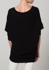 Maglione nero oversize a maglia con scollatura ampia accentuata da perline nere. Tessuto morbido, maniche corte e vestibilità rilassata.