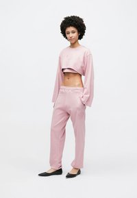 Sweatshirt rosa cropped com mangas compridas e detalhe bordado, combinado com calças de treino a condizer, com cintura elástica e detalhes bordados.