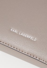 Grå lær Geldbörse med en diskret tekstur, syede kanter og et fremtrædende hvidt logo med teksten "KARL LAGERFELD" på forsiden.