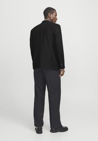 Zwarte blazer met een getailleerde pasvorm, geknipte revers en twee knopen. Gecombineerd met donkere broek en zwarte schoenen. Eenvoudig ontwerp, geen zichtbare patronen.