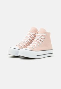 Zapatillas altas de lona rosa suave con cordones blancos, una franja negra como detalle y suela de goma; puntera texturizada y ojales metálicos.