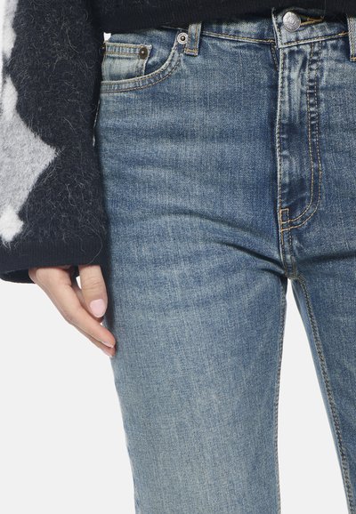 Jeans in denim blu sbiadito con un design classico, dotati di cinque tasche e cuciture discrete. La texture morbida si abbina a un maglione nero a trama.