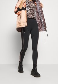 Leggings negras con franjas laterales rosas y un diseño ajustado; combinados con una chaqueta melocotón que tiene un forro de estampado de leopardo y bolsillos.