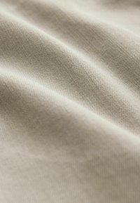 Bežna tkanina s finim, teksturiranim tkanjem, koja prikazuje meke nabore i suptilna sjenčanja, što ukazuje na debljinu i glatku završnu obradu.