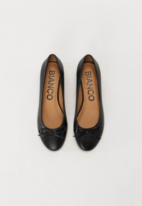 Ballerine nere realizzate in materiale sintetico liscio. Punta rotonda con un piccolo fiocco come accent. L'interno presenta una soletta color beige con il marchio "BIANCO".