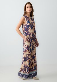 Mouwloze, cropped top en wijde broekset in een lichtgewicht stof. Kleurrijk paisleypatroon in blauw, crème en beige met een gladde textuur.