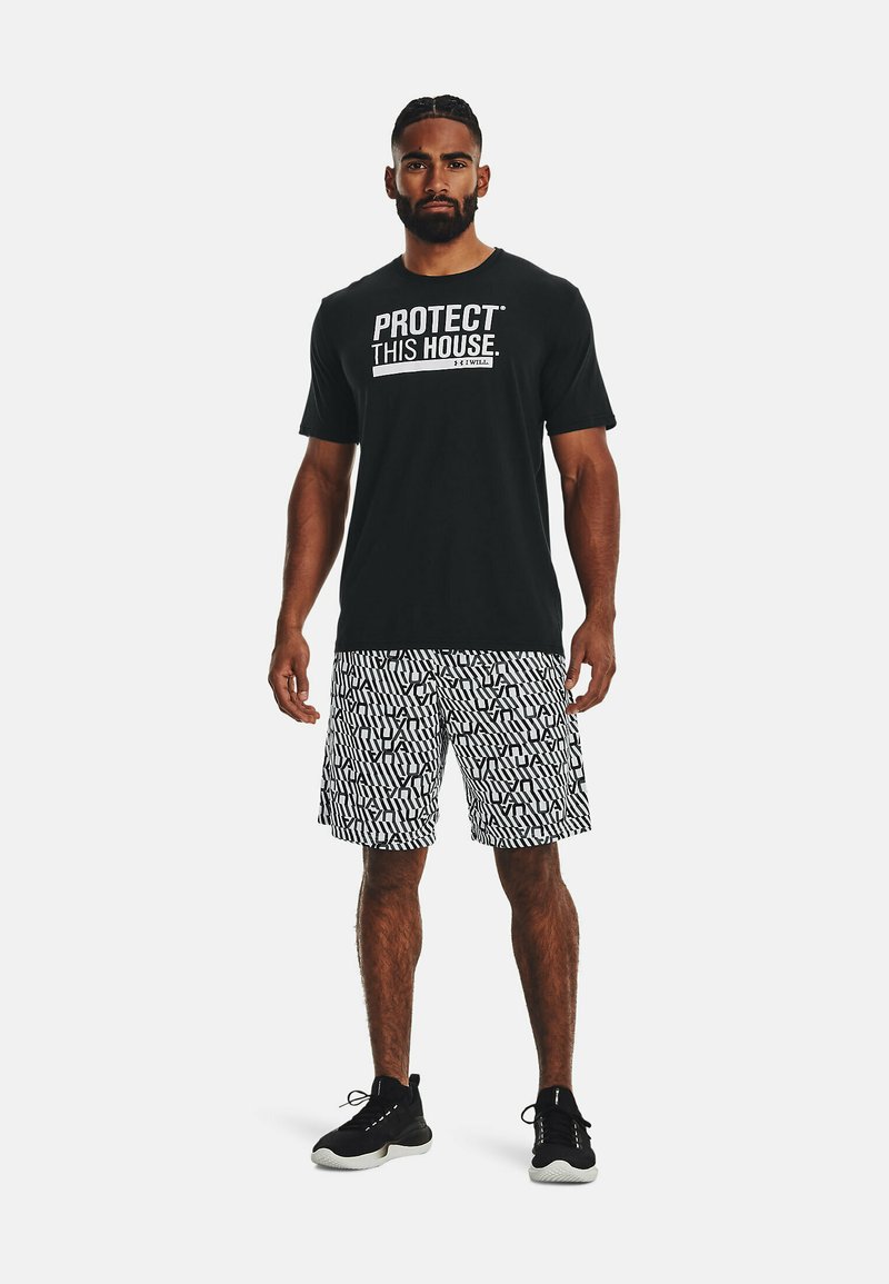 T-shirt noir à manches courtes avec le texte "PROTÉGEZ CETTE MAISON", associé à un short à motifs noir et blanc. Chaussures de sport noires.