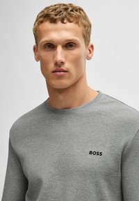 Grijze gemêleerde trui met een geribbelde afwerking. Heeft een ronde hals en een zwart "BOSS" logo op de borst. Eenvoudig, casual ontwerp.