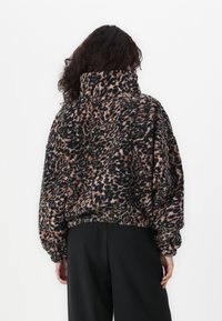 Leopard print fleece pullover with a high collar, balloon sleeves, and elastic hem. Colors include black, brown, and cream. Soft texture.