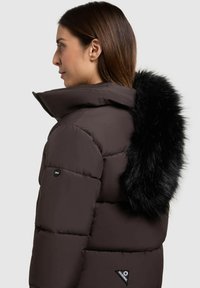 Jachetă puf, de culoare maroniu închis, cu guler înalt și o margine din blană neagră la glugă, având un patch cu logo și un design matlasat.