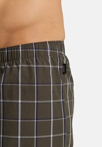 Boxers de cuadros con una cinturilla elástica, que presentan un patrón de cuadros en verde, azul marino y blanco. La tela parece suave y ligera, con una etiqueta en el lateral.