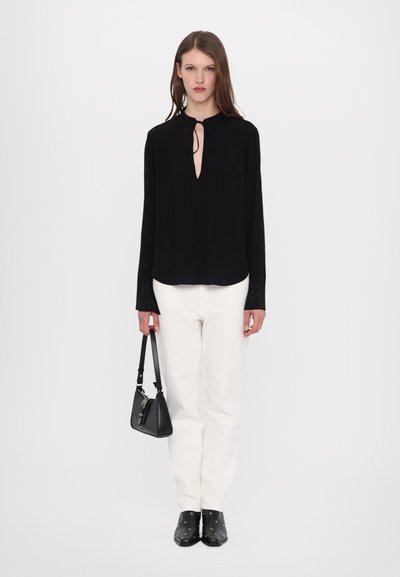 Black long-sleeve blouse with a neck tie and gathered detailing; paired with white jeans and black ankle boots featuring silver accents.
