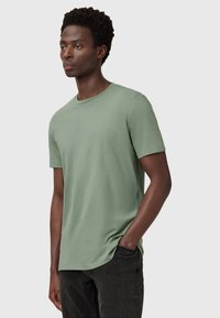 Světle zelené tričko s krátkým rukávem z měkké látky, s kulatým výstřihem a malým vyšívaným logem na hrudi.