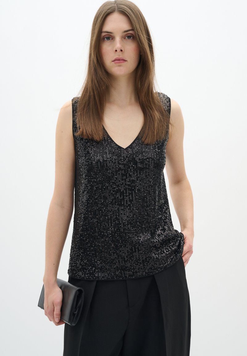 Top nero senza maniche con scollatura a V, ricoperto di paillettes, con una vestibilità comoda e una superficie liscia. Abbinato a pantaloni neri e una pochette.