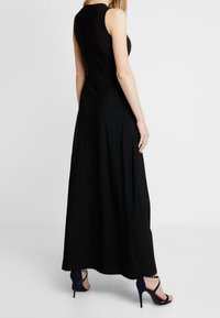 Musta maksimekko, jossa on hihaton muotoilu ja sileä materiaali. Mekolla on vartalonmyötäinen yläosa, ja se laskeutuu lattiaan asti. Yhdistetty sinisten korkokenkien kanssa.