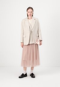 Lys beige lin blazer over en kremfarget topp, parret med et gjennomsiktig rosa tyllskjørt. Svarte loafers og en liten rosa håndveske kompletterer antrekket.