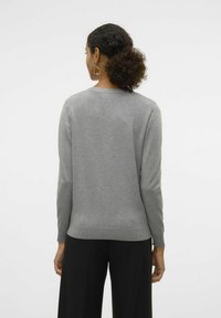 Grå pullovertröja med långa ärmar, ribbat avslut och detalj vid halsringningen. Slät textur; bärs med svarta byxor och stora hoopsörhängen.