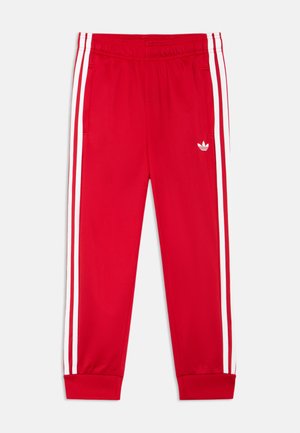 Røde treningsbukser med hvite sidelister, elastisk midjebånd, mansjetter ved ankler og liten hvit Adidas-logo på venstre lår.