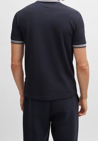 Marinblå kortärmad polo med en texturerad yta, som har en kontrasterande ribbad krage och manschetter med subtila randiga detaljer.