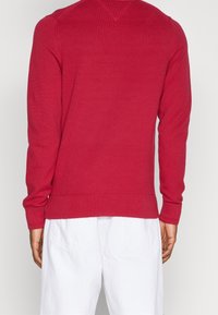 Maglione a coste rosso con maniche lunghe, scollatura a V sul retro e orlo aderente. Il tessuto testurizzato offre una vestibilità aderente.
