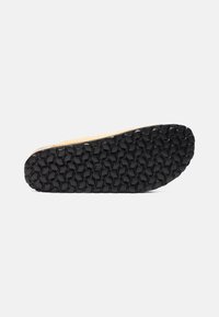 Sort gummisål med et struktureret mønster af cirkulære indtryk, med en naturlig farve kant øverst.