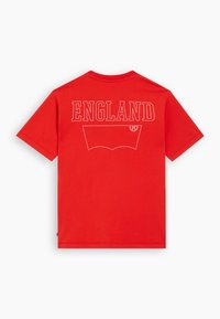 Crvena pamučna majica s kratkim rukavima, koja sadrži riječ "ENGLAND" u bijelom slovlju na leđima, s velikim grafičkim motivom ispod. Standardni kroj.