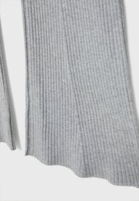 Tissu en maille côtelée grise avec une texture douce, présentant des lignes verticales et des bords légèrement évasés, adapté à une tenue décontractée.