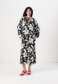Laivansiniset mekko, jossa on suuri valkoinen kukkakuosi, pitkät puffihihat ja nauhatasku. Paritettuna punaisilla remmi-Pumpsseilla, joissa on terävä kärki.