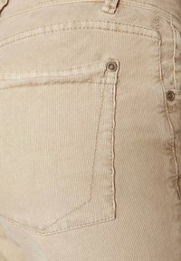 Beiga manchestygbyxor med subtila vertikala åsar, en bakficka med en metalldocka och förstärkningsstygn längs sömmarna.