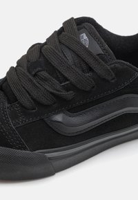 Baskets noires avec une tige en daim, des lacets texturés, des accents lisses et une semelle en caoutchouc légèrement courbée au niveau des orteils.
