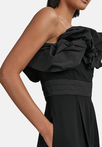 Crna haljina koja se ističe strukturiranim, naboranim dekoltea, uskim korzetom sa horizontalnim prugama i bočnim džepovima u lepršavom dizajnu suknje.