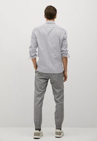 Gestreepte, lange mouwen shirt in wit en marineblauw. Grijze, taps toelopende broek met elastische boorden en zijzakken. Model draagt sneakers.