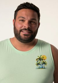 Jasnozielona koszulka bez rękawów z okrągłym dekoltem, zdobiona haftem przedstawiającym trzy palmy i słońce na lewej stronie klatki piersiowej.