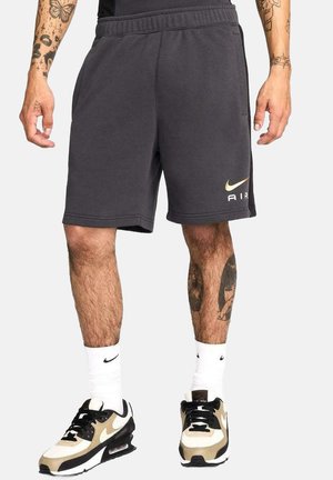 Pantalones cortos Nike de color gris oscuro con un logo "AIR" dorado, cinturilla elástica, bolsillos laterales y un ajuste relajado, combinados con zapatillas negras y beige.