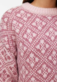 Pull en tricot rose présentant un motif géométrique dans des nuances variées de rose, avec un col rond côtelé et une texture douce et pelucheuse.