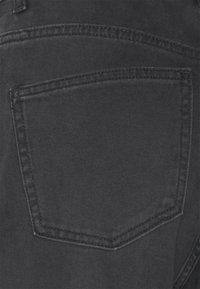 Gros plan d'une poche arrière de jean en denim noir avec des coutures visibles et la texture du tissu.