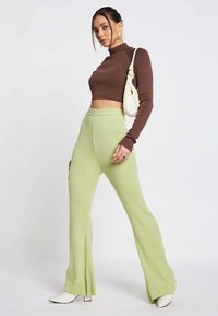 Bruine ribbelige korte turtleneck, lichtgroene ribbelige uitlopende broek met splitjes, witte haklaarzen en een witte gebogen handtas.